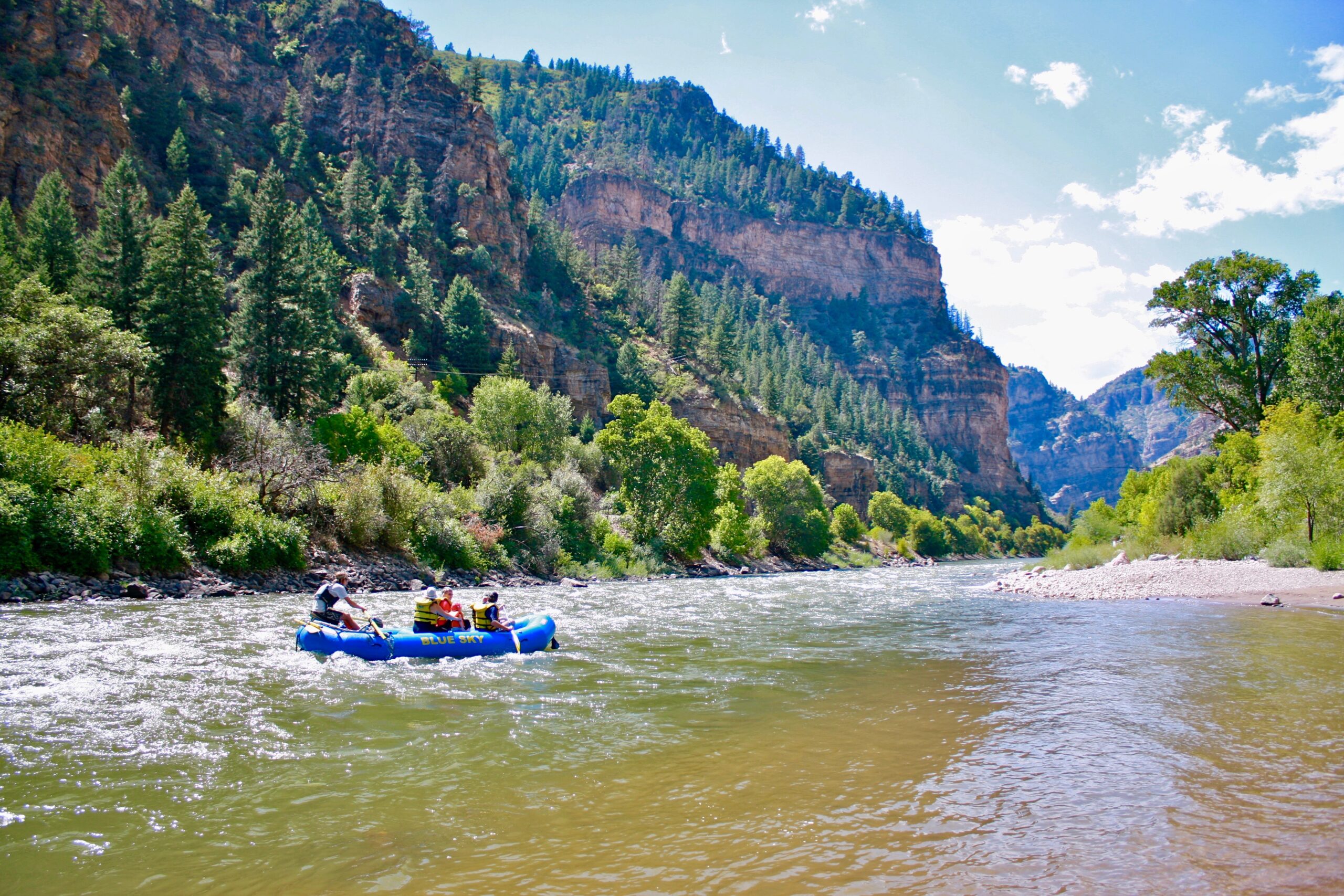 This serene photo captures a boat gracefully floating on the calm Class II waters of the river. The surroundings unfold with a perfect view of canyon walls and lush vegetation that encircle the river, creating a tranquil and picturesque scene.