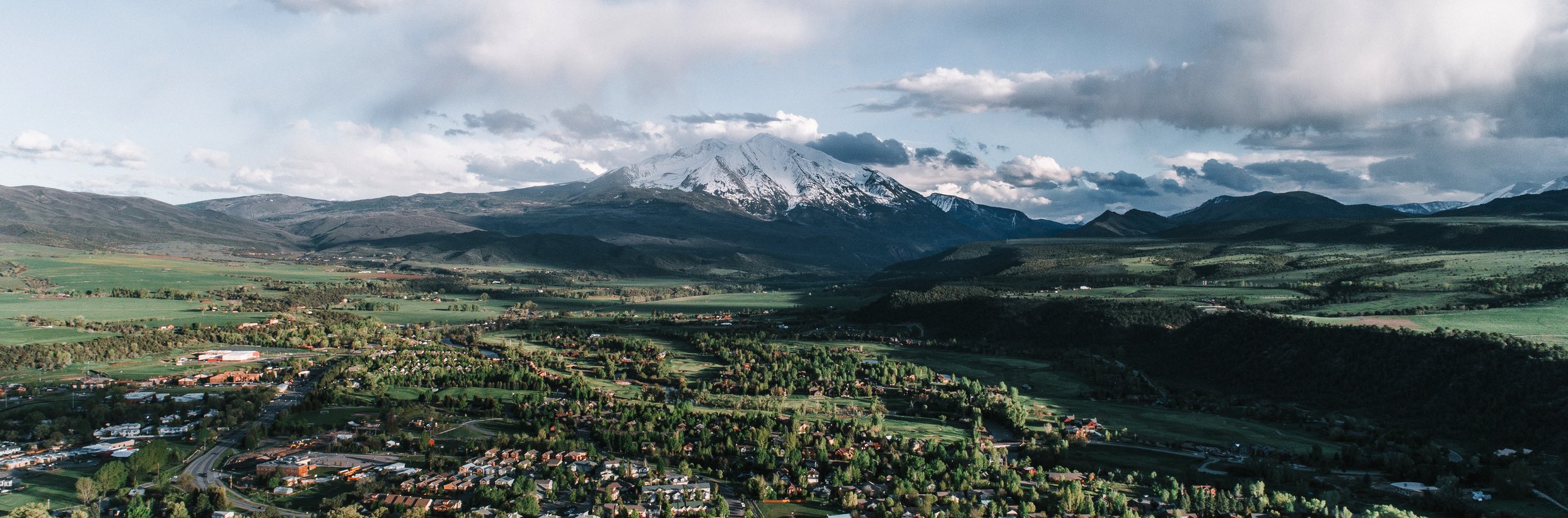 An image capturing the snowcapped majesty of Mount Sopris, overlooking the town of Carbondale below, framed by vibrant green trees.