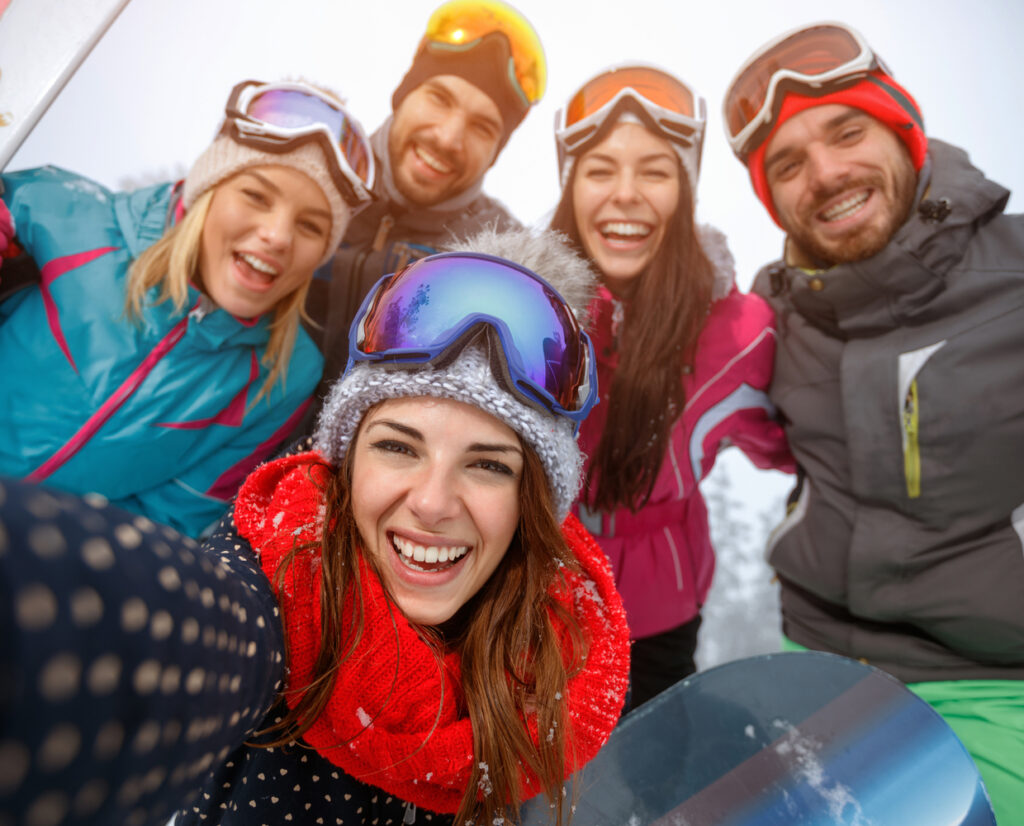 A cheerful group of friends pause for a photo while snowboarding on the mountain. Their vibrant, brightly colored winter attire stands out, and the big smiles on their faces reflect the joy and excitement of their snowboarding adventure.
