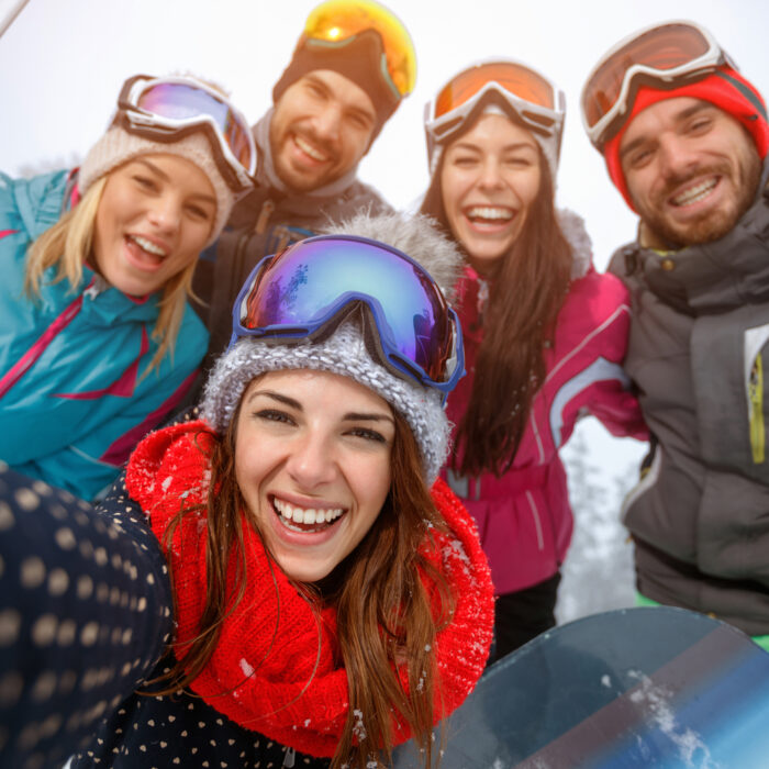 A cheerful group of friends pause for a photo while snowboarding on the mountain. Their vibrant, brightly colored winter attire stands out, and the big smiles on their faces reflect the joy and excitement of their snowboarding adventure.
